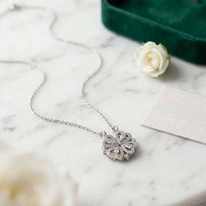 Silver transformable necklace displayed on marble surface with four crystal hearts joined into a sparkling four-leaf clover pendant.