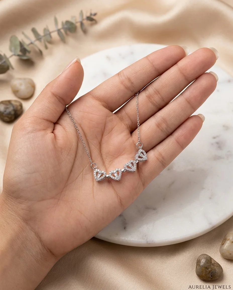 Hand holding a delicate silver necklace featuring four crystal heart charms arranged in a horizontal row.
